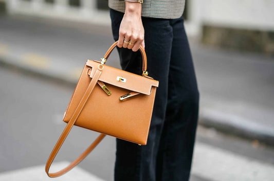 alt="Main tenant un sac ressemblant à un modèle de luxe, fond d’atelier flou"
